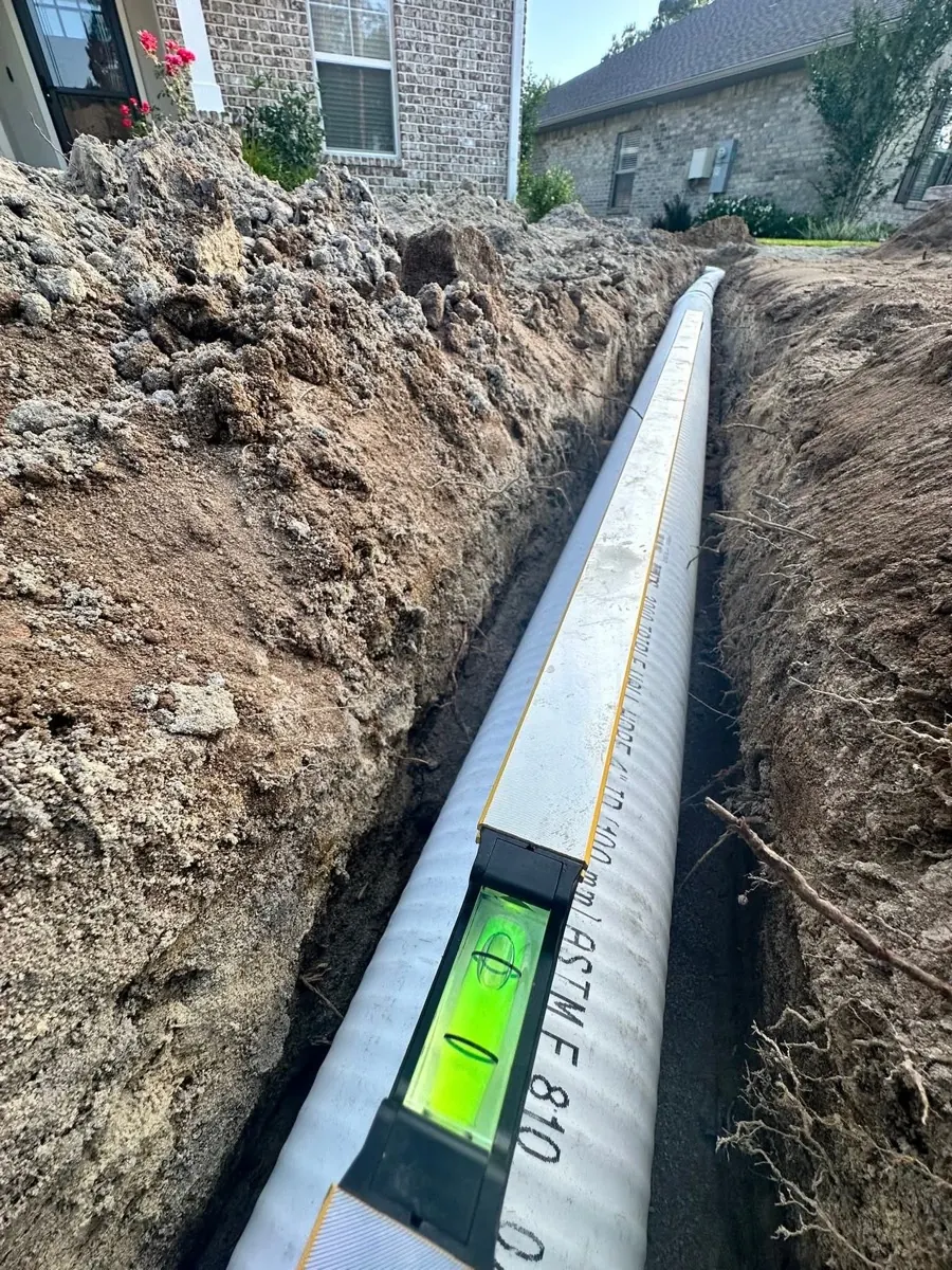 French drain installation with level showing proper slope - HT Outdoor Living